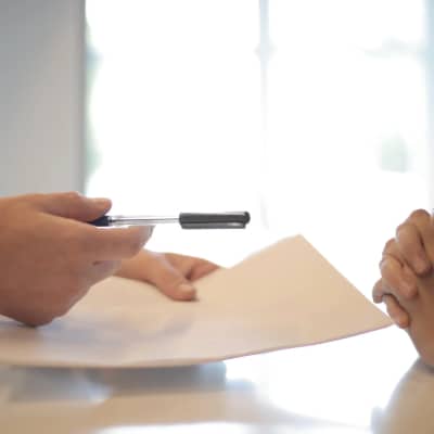 hands over a desk, one holding paper documents